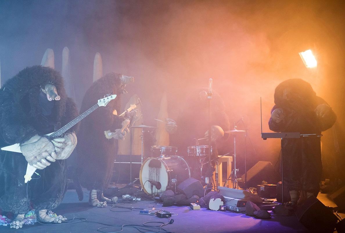 Czwórka muzyków w strojach kretów grająca na instrumentach. Dookoła nich unosi się dym.