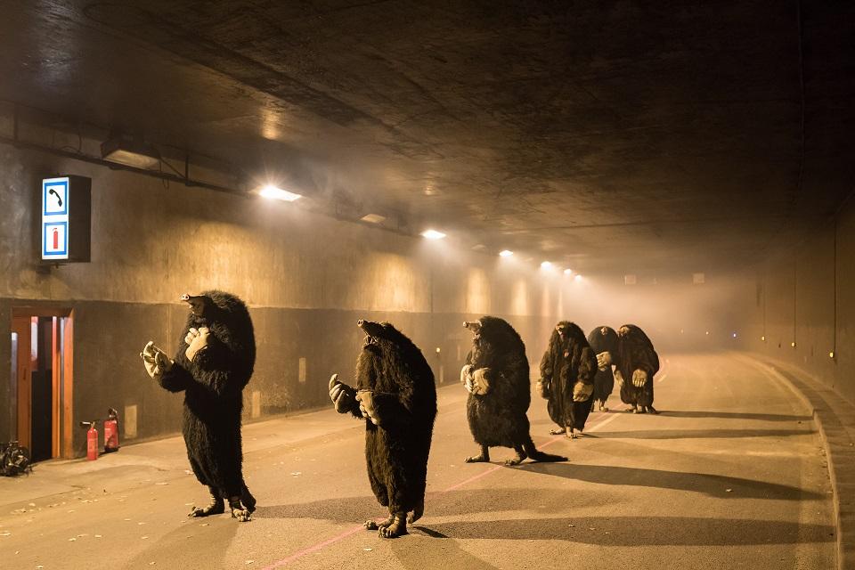 Sześcioro artystów w strojach kretów w długim oświetlonym tunelu.