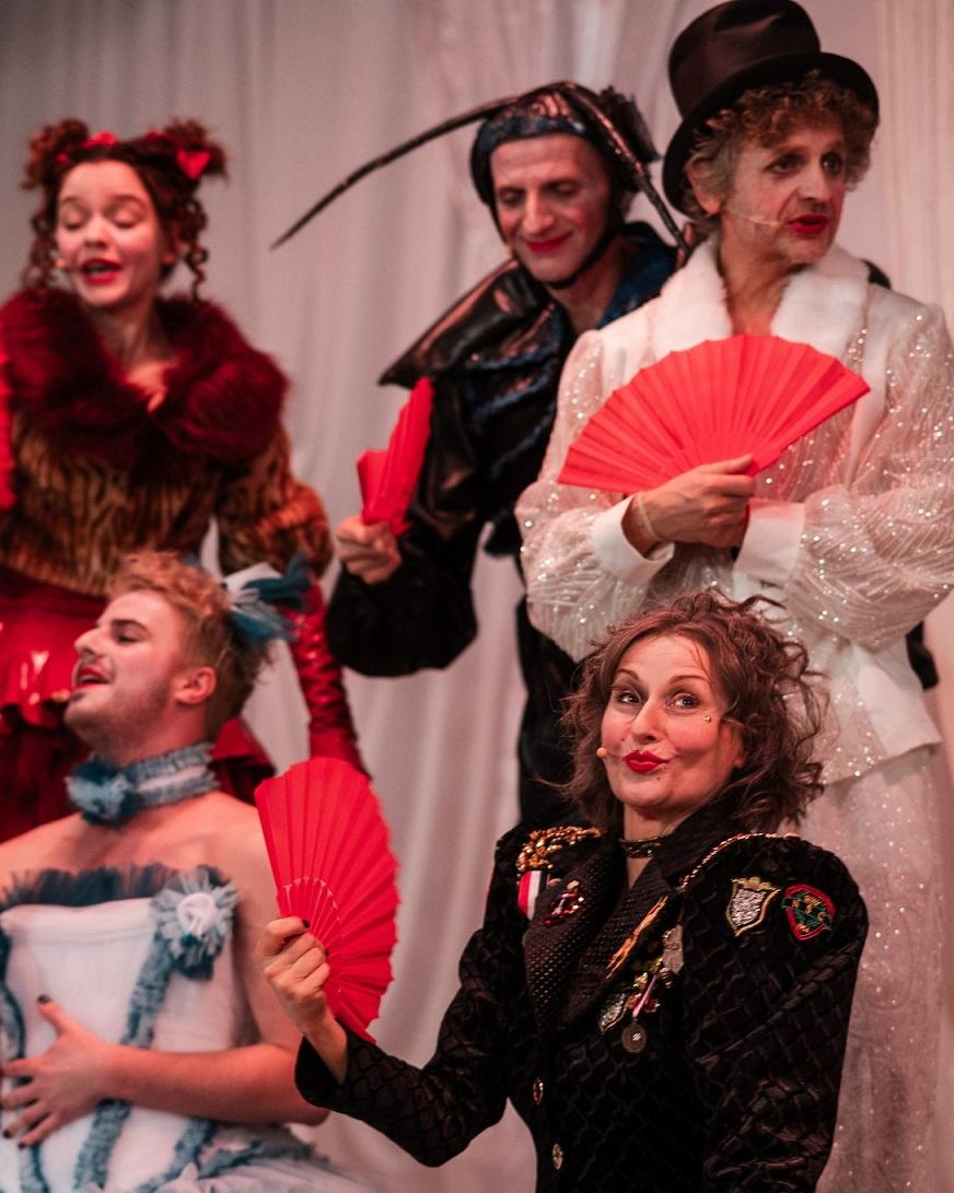 Grupa aktorów w różnych kostiumach trzymająca czerwone wachlarze.